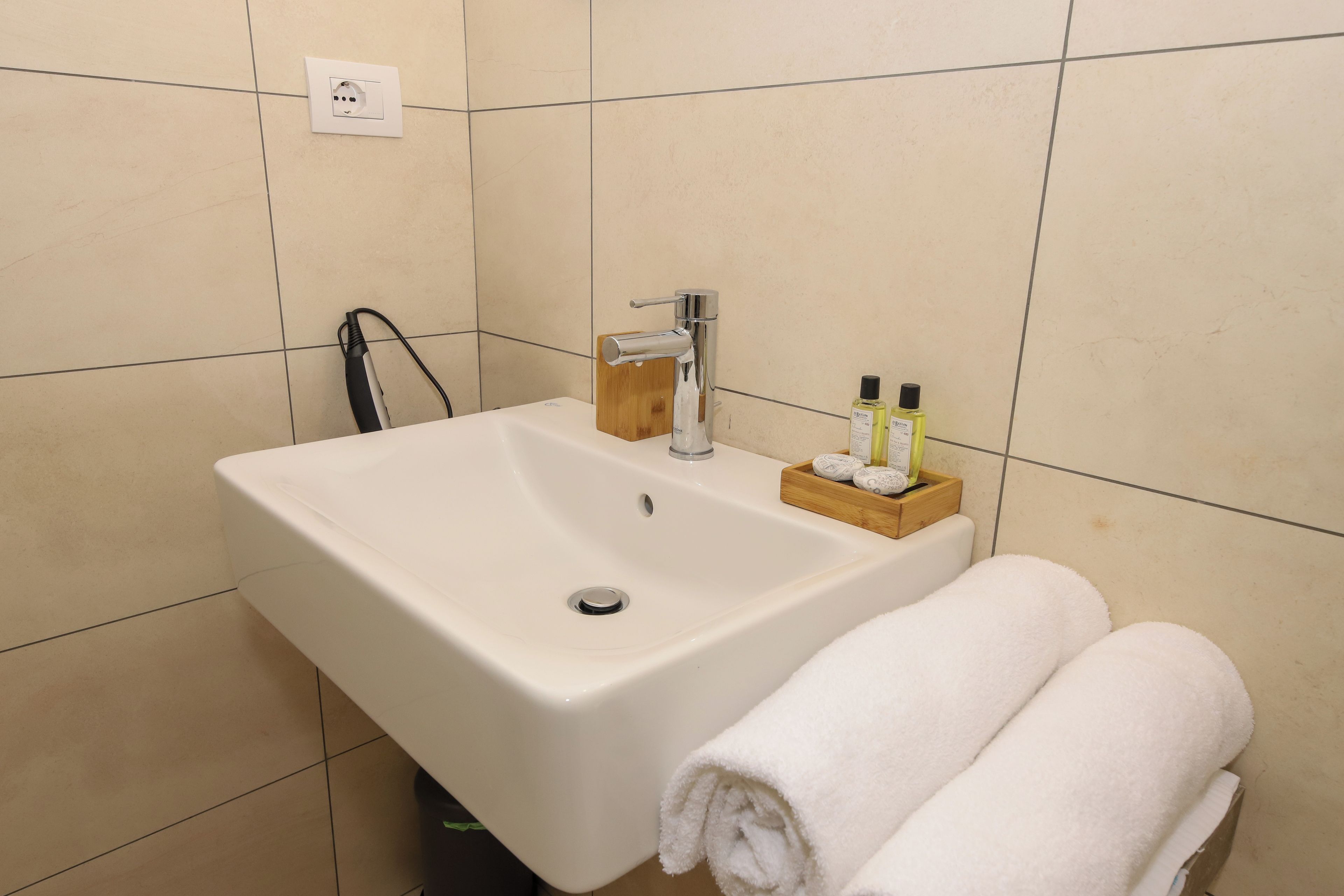 A bathroom with a white sink, a faucet, a towel rack with towels, and toiletries on a wooden tray.