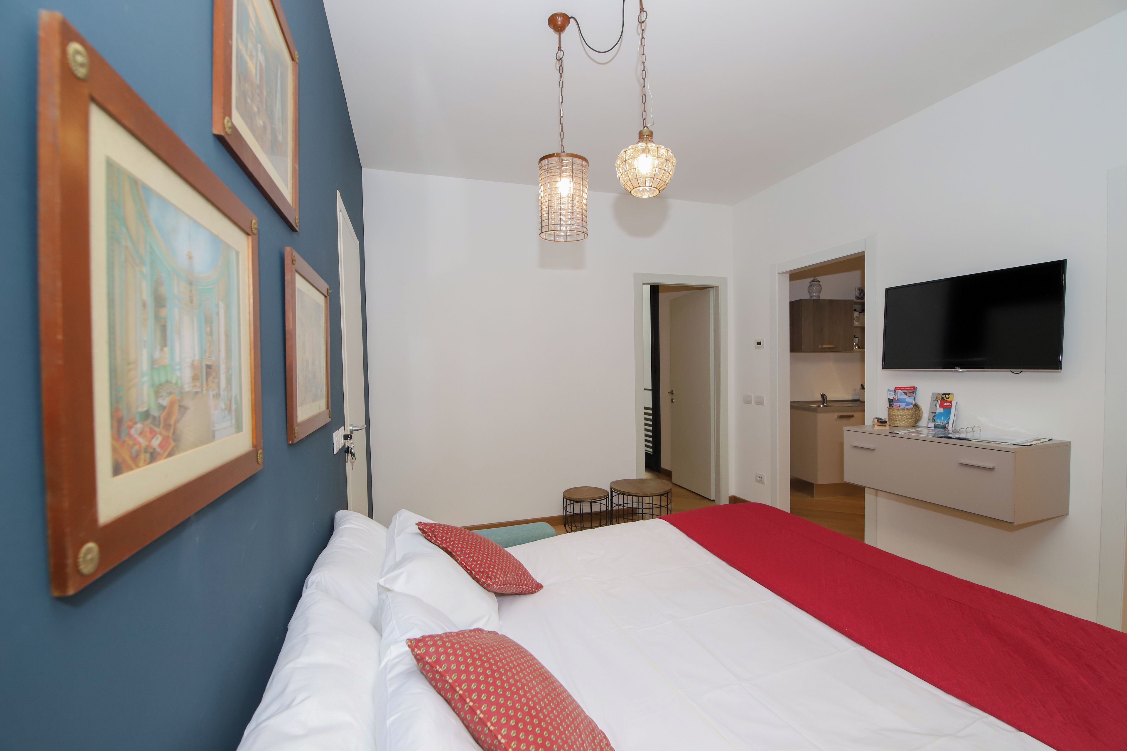 A hotel room with a bed, a TV, a desk, and a kitchenette.