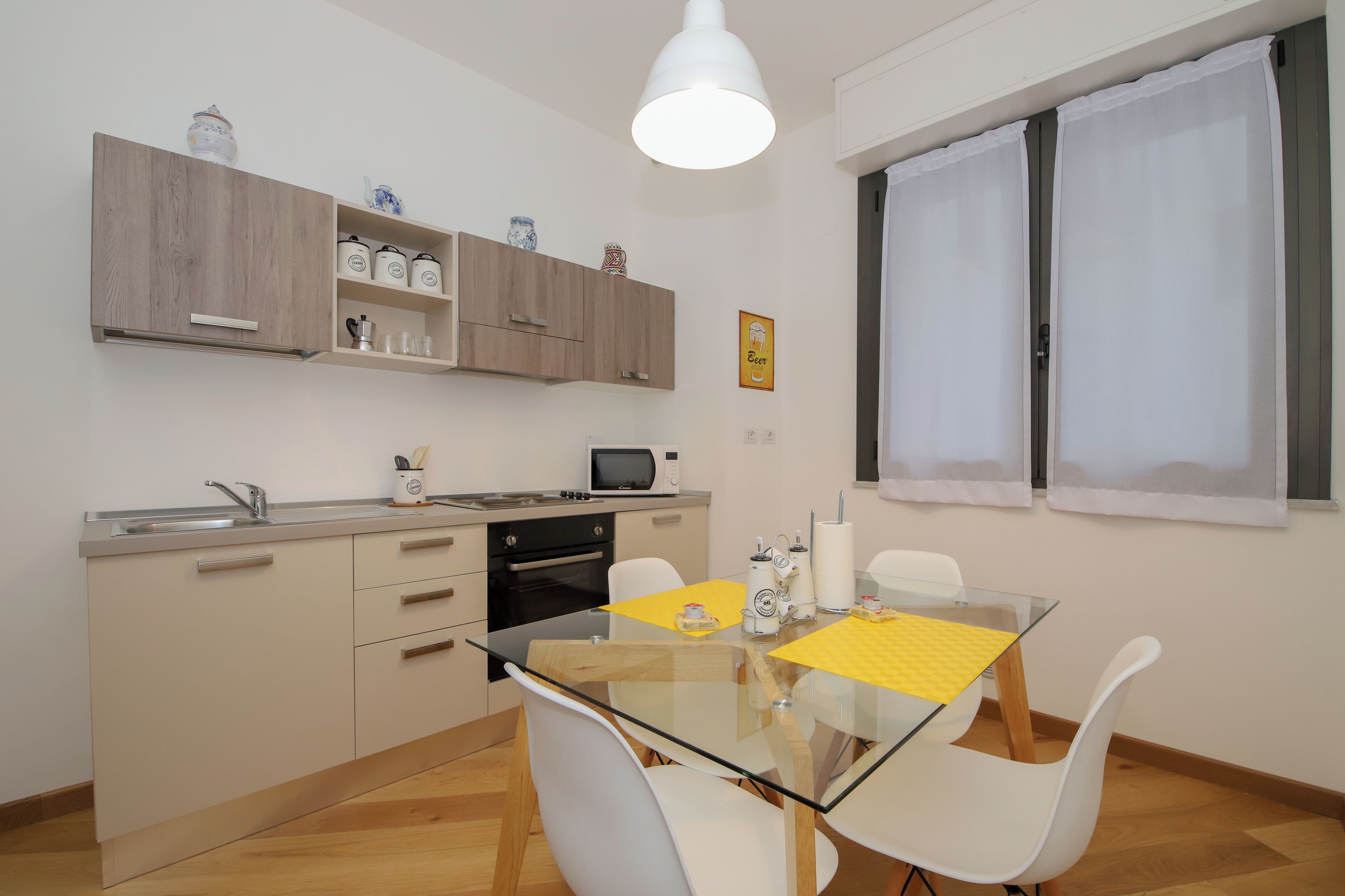 Una cocina moderna con armarios de madera, microondas y un comedor con mesa de vidrio y sillas blancas.