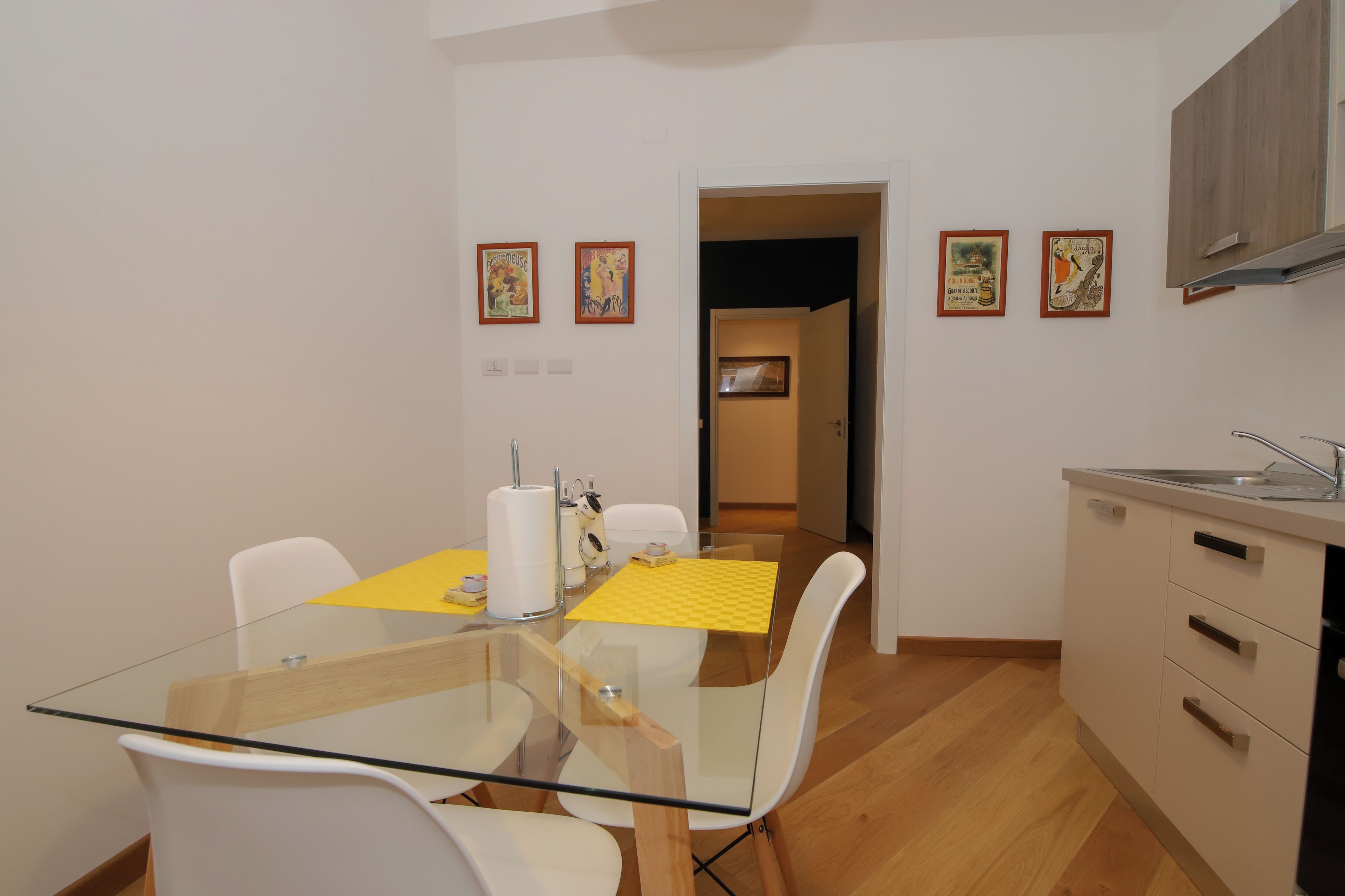 Een moderne keuken met een glazen eettafel, witte stoelen en houten kastjes.
