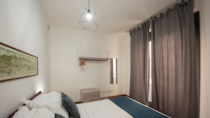 A bedroom with a bed, a dresser, a hanging light fixture, and a window with curtains. - U Genova (Genoa)