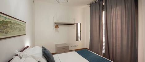 A bedroom with a bed, a dresser, a hanging light fixture, and a window with curtains.