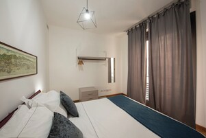 Un dormitorio con cama, cómoda, lámpara colgante y ventana con cortinas.