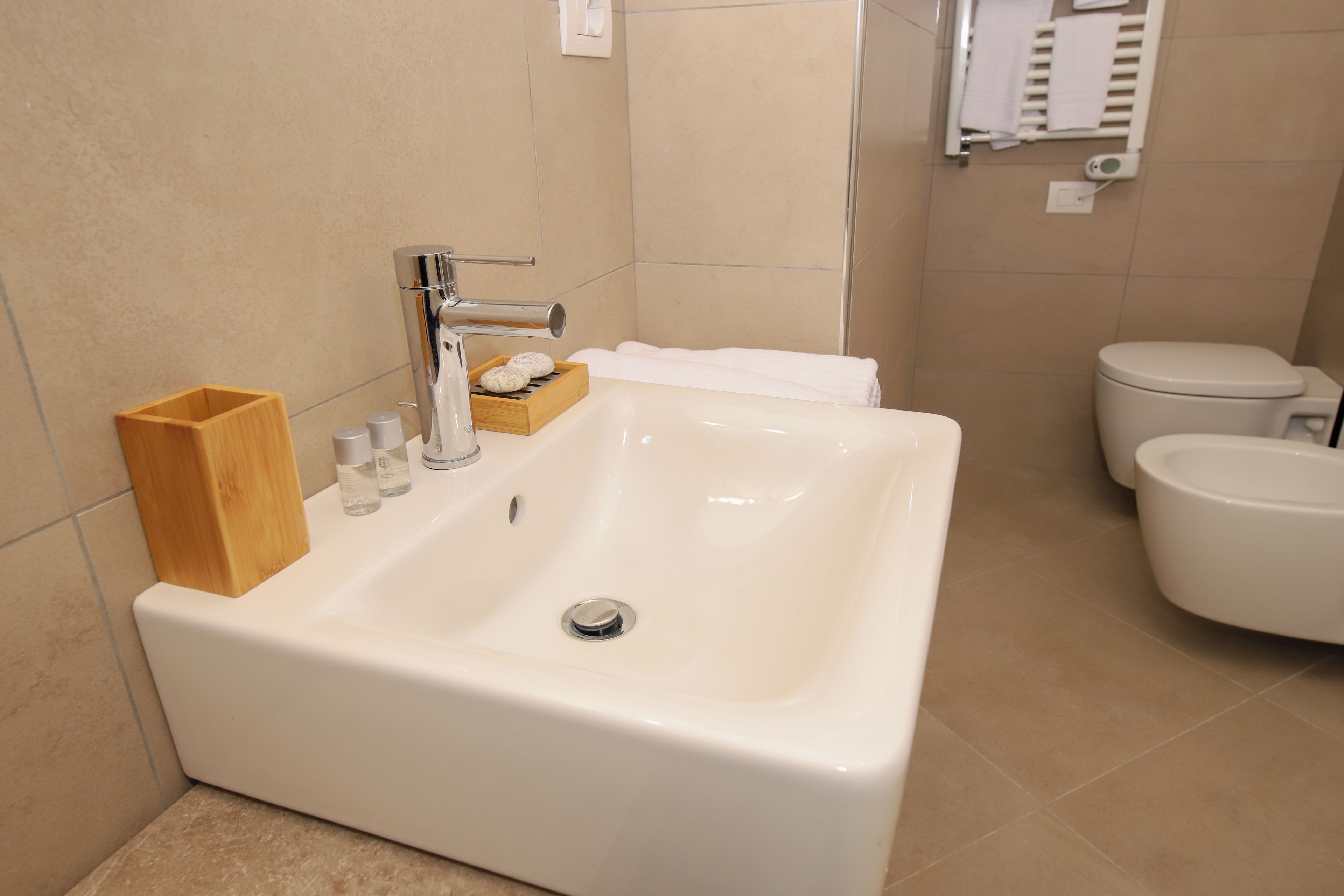 A bathroom with a white sink, a wooden soap dish, and a toilet.