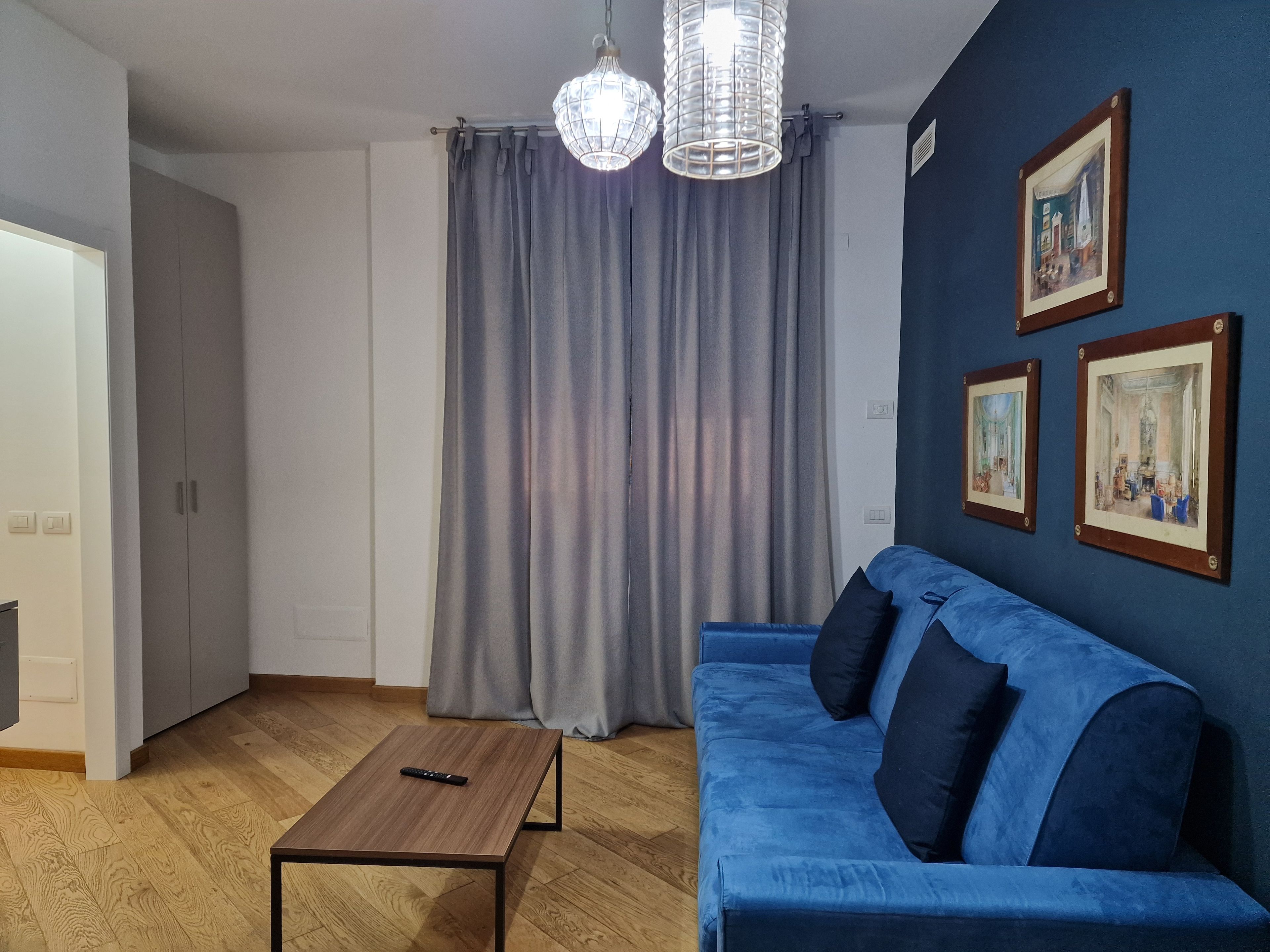 A room with a blue sofa, a wooden coffee table, grey curtains, and two wall-mounted pictures.