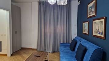 A room with a blue sofa, a wooden coffee table, grey curtains, and two wall-mounted pictures.