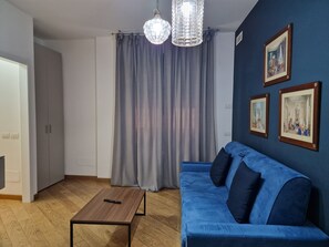 A room with a blue sofa, a wooden coffee table, grey curtains, and two wall-mounted pictures.