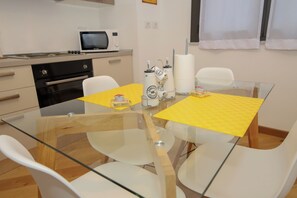 A modern kitchen with a glass table, white chairs, a microwave, and a stove. - U Genova (Genoa)