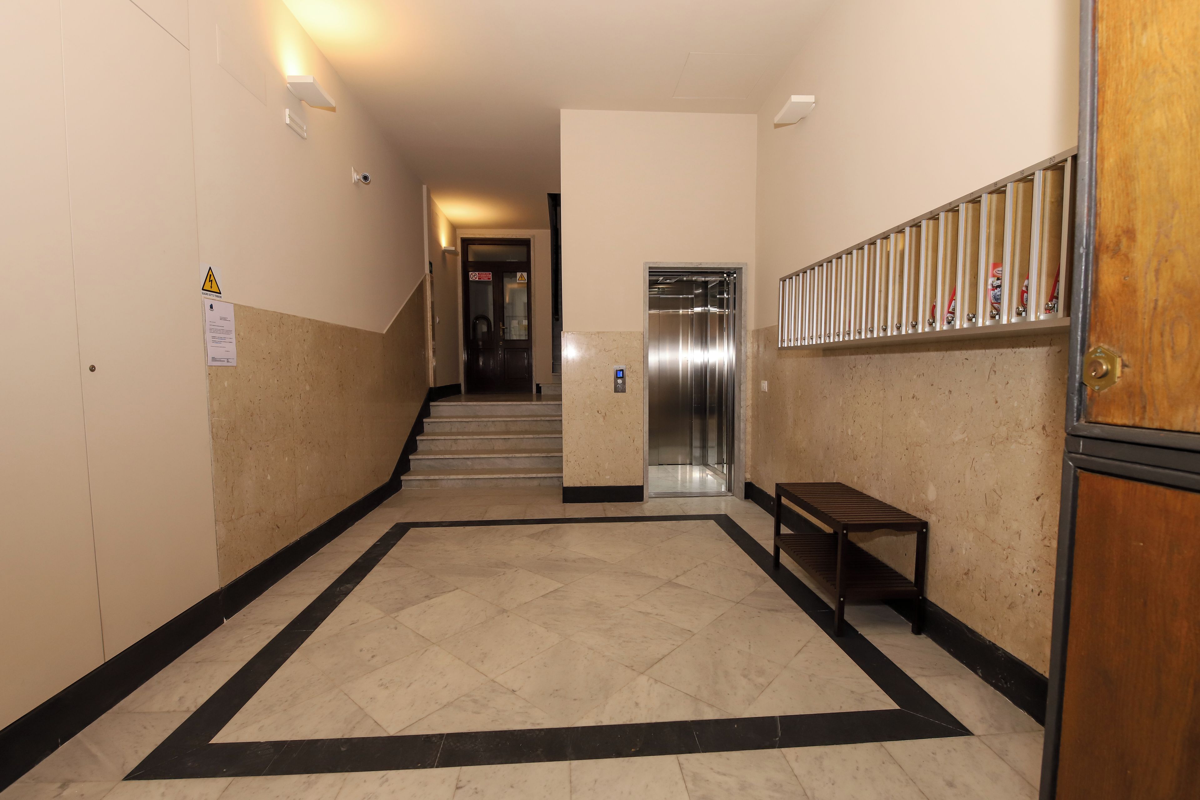 Käytävä, jossa on laatoitettu lattia, penkki ja hissi.