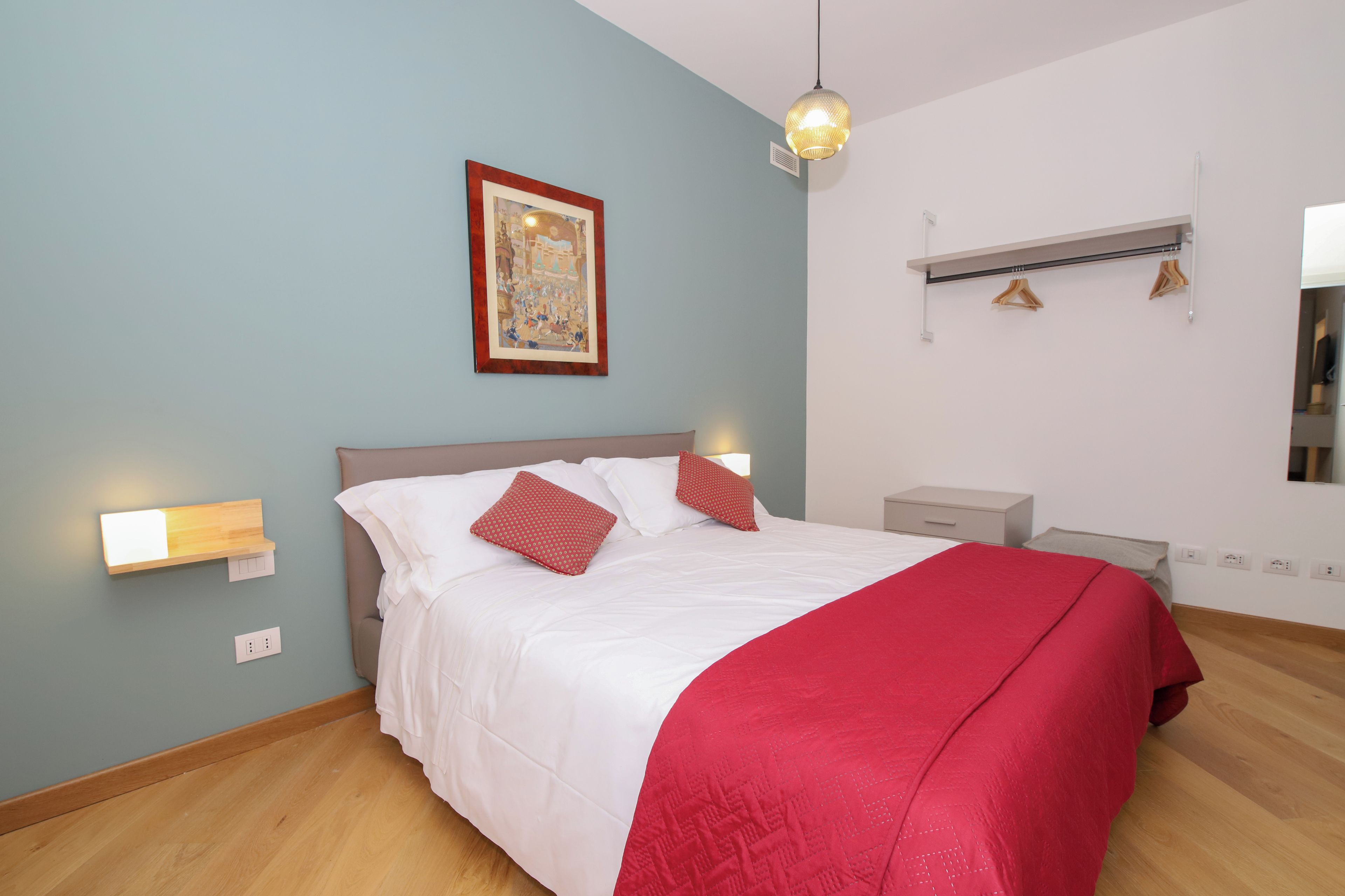 Un dormitorio con cama, mesitas de noche, lámpara colgante, aire acondicionado instalado en la pared y un cuadro enmarcado.