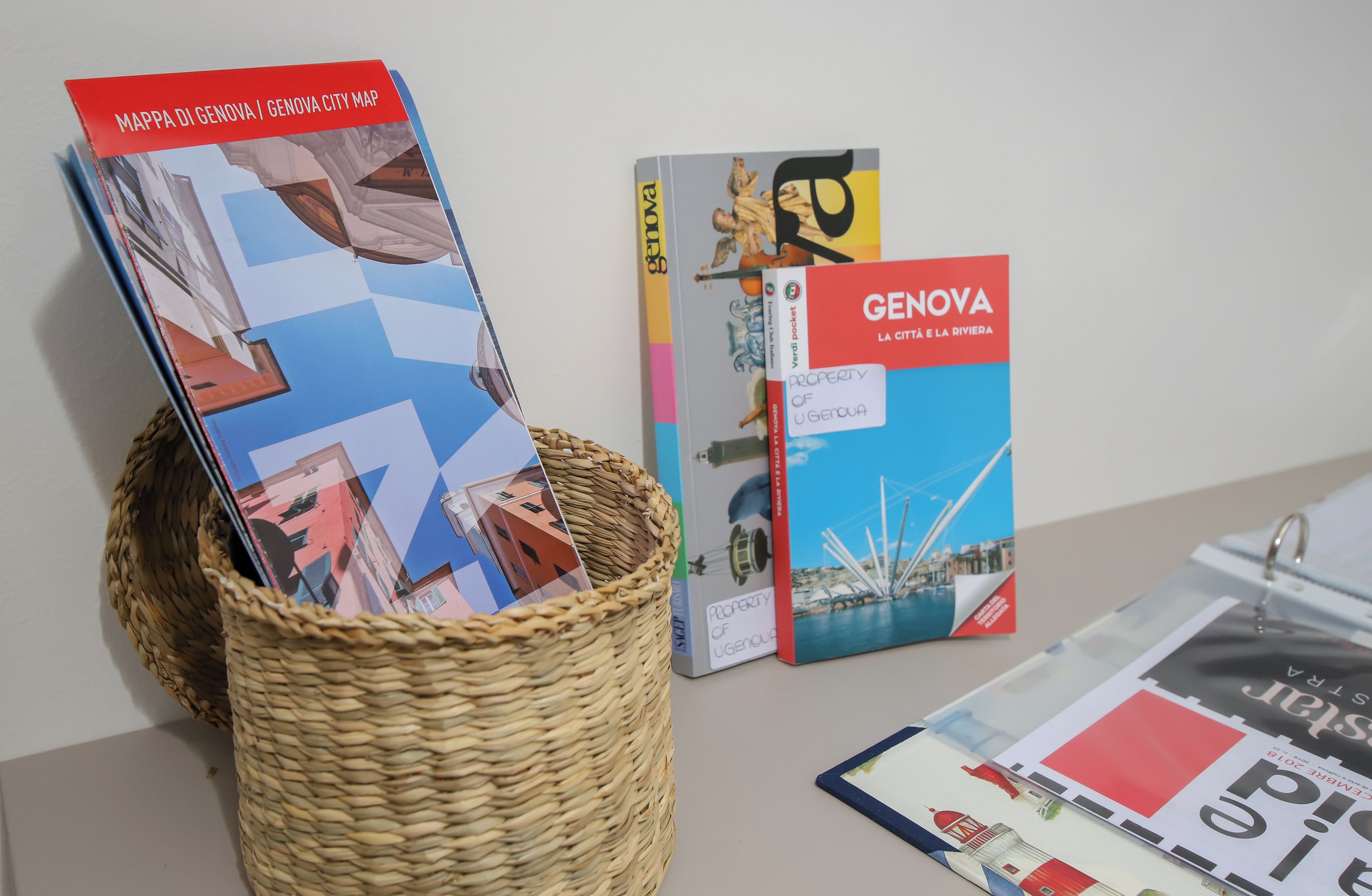 A basket containing a map and a book titled 'GENOVA LA CITTÀ E LA RIVIERA' with a cityscape illustration.