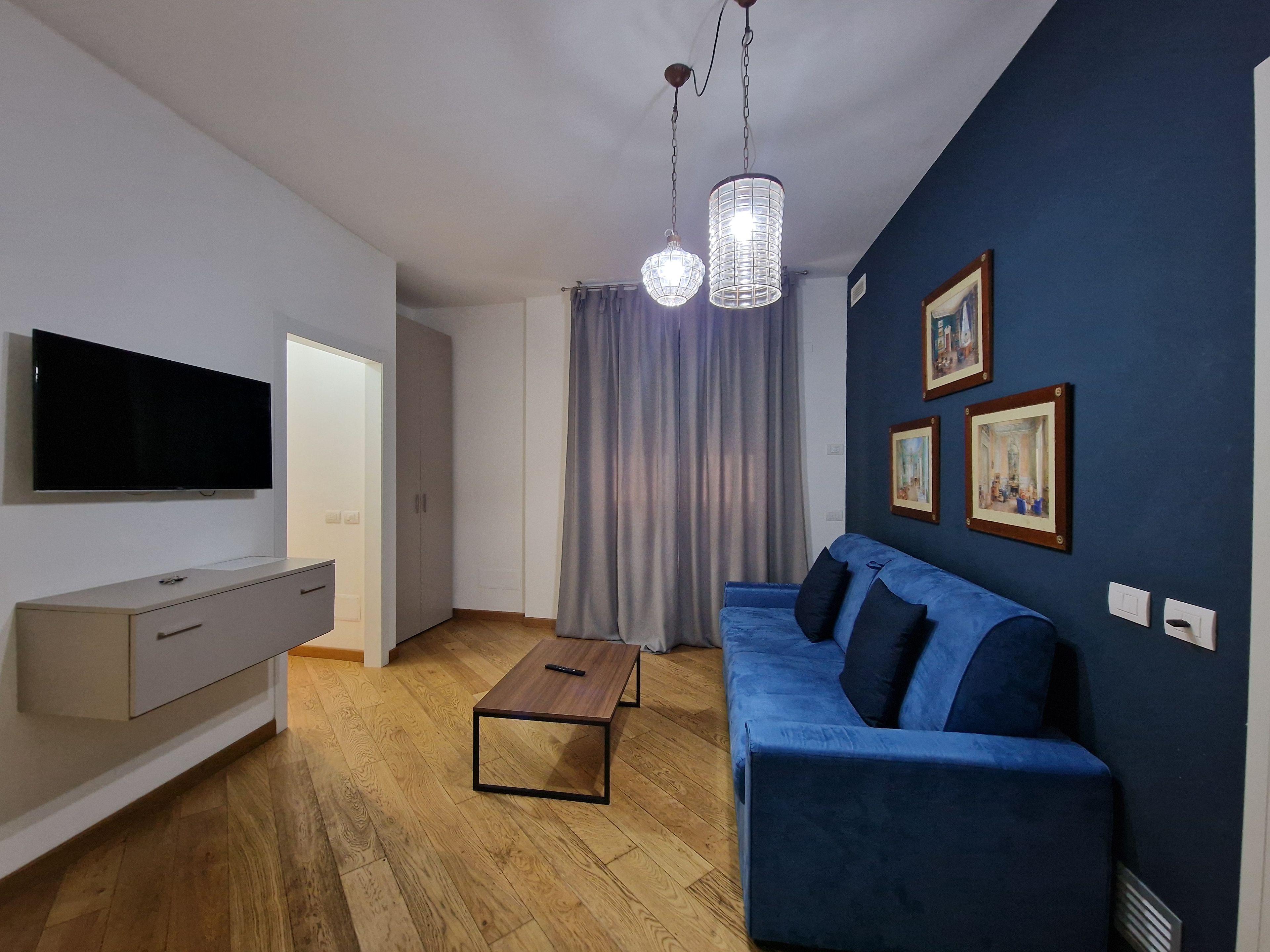 Una sala moderna con televisor de pantalla plana, un sofá azul, una mesa de centro de madera y una lámpara colgante.