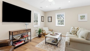 A living room with a flat-screen TV, a coffee table, a sofa, a bookshelf, and a potted plant.