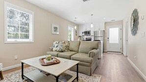 A modern living room with a sofa, a coffee table, and a kitchen area with appliances. - Treehouse at BootLegger Cove (Bluffton)