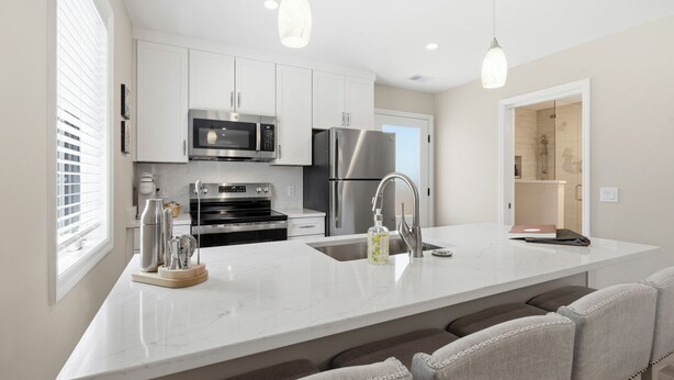 A modern kitchen with white cabinetry, stainless steel appliances, and a marble countertop. - Treehouse at BootLegger Cove (Bluffton)