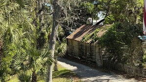 A rustic building with a sloped roof, surrounded by lush greenery and trees. - Treehouse at BootLegger Cove (Bluffton)