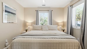 A bedroom with a bed, two bedside tables, a wall-mounted air conditioner, and a window with curtains.