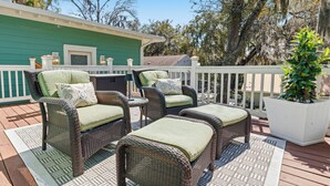 An outdoor deck with wicker furniture, a white railing, and a green building in the background. - Treehouse at BootLegger Cove (Bluffton)