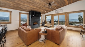 A cozy living room with a fireplace, leather sofas, and large windows offering a scenic view. - 224 GCR 4034 Luxury 4 bedroom home, lake views, private hot tub (Grand Lake)