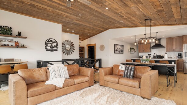 A spacious living area with two leather sofas, a white shag rug, wooden ceiling, and a kitchen in the background. - 224 GCR 4034 Luxury 4 bedroom home, lake views, private hot tub (Grand Lake)