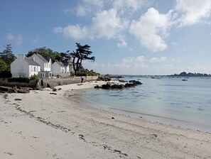 En ejendom ved kysten med strand, hvidt hus og stenet kystlinje.