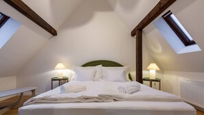 A bedroom with a high ceiling, a sloped roof, two bedside lamps, a bed with white linens, and a bench in the corner. - Cosy 1-BR for two · central Zürich · self check-in (Zürich)