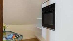 A kitchen with a built-in oven, a small table with a vase, and a wooden floor. - Cosy 1-BR for two · central Zürich · self check-in (Zürich)