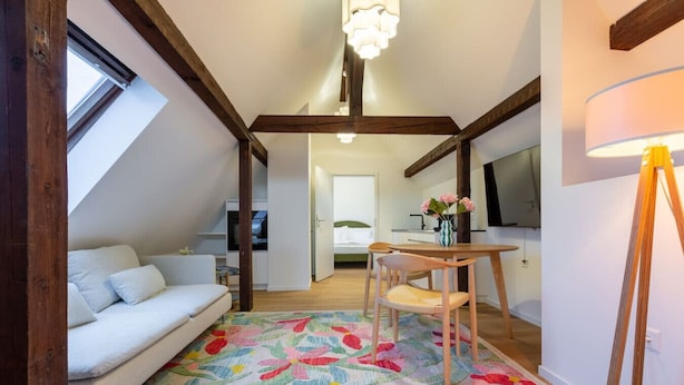 A cozy loft-style room with a sloped ceiling, a white sofa, a wooden dining table with chairs, and a colorful rug. - Cosy 1-BR for two · central Zürich · self check-in (Zürich)