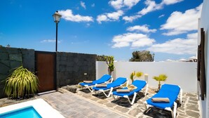 A pool area with lounge chairs, a stone wall, and a lamp post. - Vacation Villa 'Rubicon' with Sea View, Wi-Fi and Air Conditioning (Yaiza)