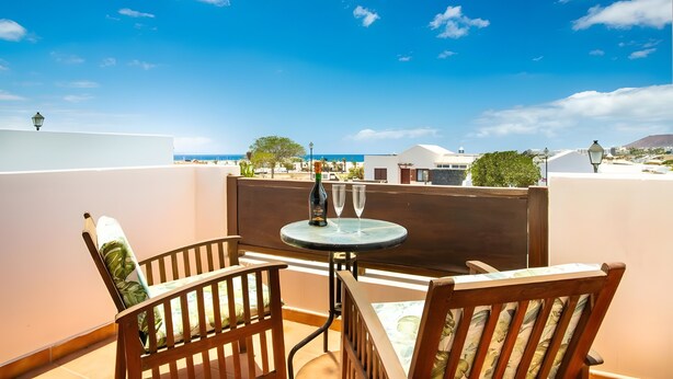 A balcony with a table and chairs, a bottle of champagne, and a view of the sea and buildings. - Vacation Villa 'Rubicon' with Sea View, Wi-Fi and Air Conditioning (Yaiza)
