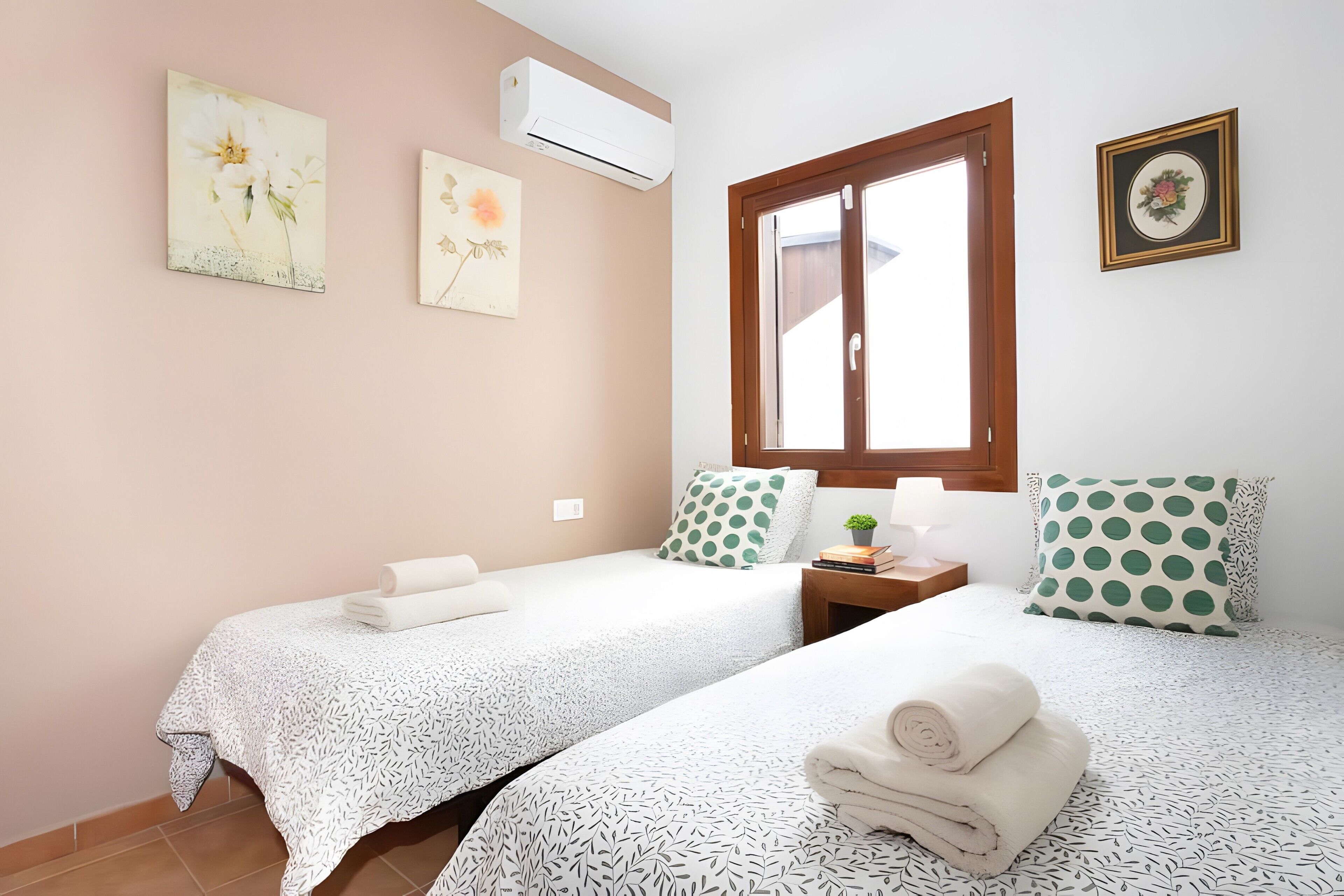 A room with two beds, a window, wall art, and an air conditioner.