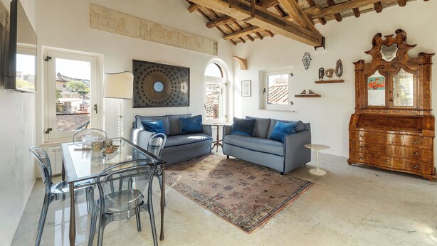 A spacious living room with a high wooden ceiling, a glass dining table with chairs, two sofas with blue cushions, a wooden cabinet, and a large mirror. - Casa Adriana, a Burghesius home (Roma)