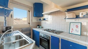 A modern kitchen with blue cabinets, a stainless steel sink, a built-in oven, and a window overlooking a rooftop. - Casa Adriana, a Burghesius home (Roma)