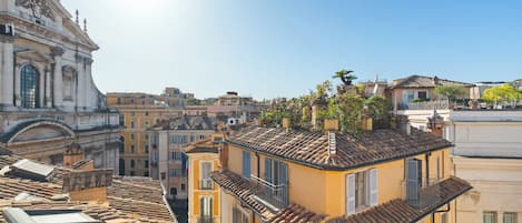 A cityscape with a prominent historical building, terracotta-roofed buildings, and a clear sky.