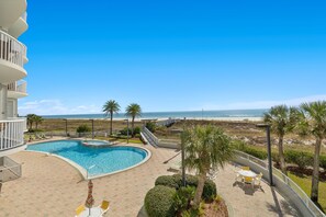 A pool area with a view of the beach, surrounded by palm trees and a building with balconies. - Beach Front in Perdido Key, Pool, Hot tub, Balcony (Pensacola)