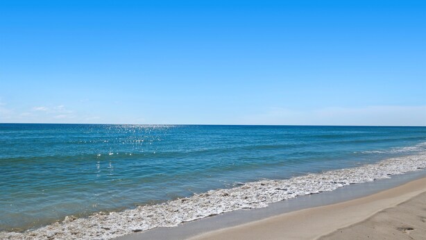 Une plage avec une eau d’un bleu limpide et un rivage sablonneux.
