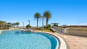 Une piscine à l’eau d’un bleu cristallin, entourée de palmiers et bordée d’une allée pavée.