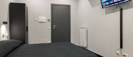 Quarto de hotel moderno com uma cama grande, uma TV de tela plana na parede, uma porta e um radiador.