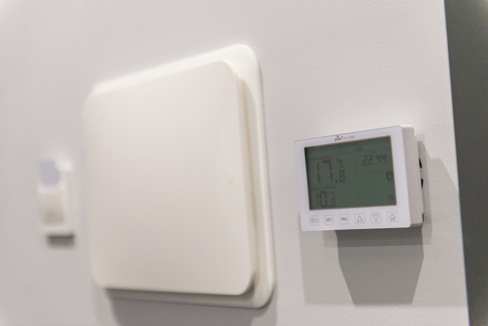 Termostato con pantalla digital en una pared, mostrando una temperatura de 17,8°C y la hora 22:44.