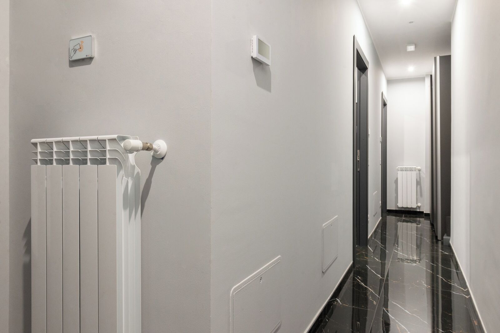A modern hallway with a radiator, a control panel, and a door leading to another room.