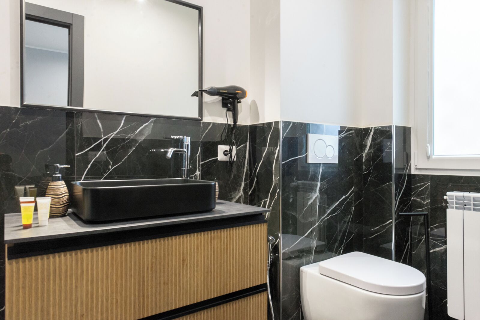 A modern bathroom with a black marble sink, a handheld hair dryer, and a toilet.