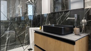 Un baño moderno con un lavabo negro, paredes de mármol y un mueble de tocador de madera.