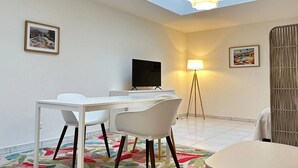 En moderne stue med spiseplads, et fladskærms-TV, en gulvlampe og et stort vindue med ovenlys.