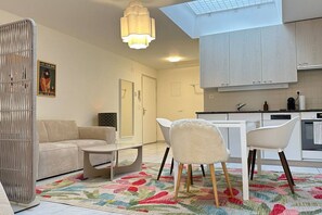 A modern living room with a sofa, a small table, and a chair. There is a kitchen area with cabinets and a countertop. A decorative rug is on the floor. - Stylish modern studio for two in Zürich (Zürich)