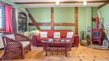 Ein Zimmer mit einem roten Sofa, Korbstühlen, einem Glastisch, Holzboden und einem roten Herd.