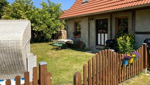Ett hus med ett rött tegeltak, ett trästaket och en trädgård med ett bord och stolar.