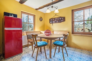 Een keuken met een rode koelkast, een ronde houten tafel met blauwe stoelen met kussens, en een raam met uitzicht op bomen.