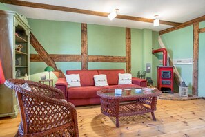 Een gezellige woonkamer met een rode bank, rieten stoelen, een glazen salontafel en een houten vloer.