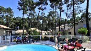 Zona de piscina con sillas de descanso y una alberca rodeada de árboles altos.