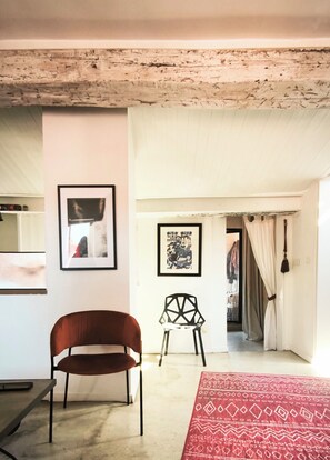 A room with a wooden ceiling, a brown chair, a white chair, a red patterned rug, and two framed pictures on the wall. - New! Charm, ideal location, 2 bedrooms, air conditioning, balcony with view. (Sète)